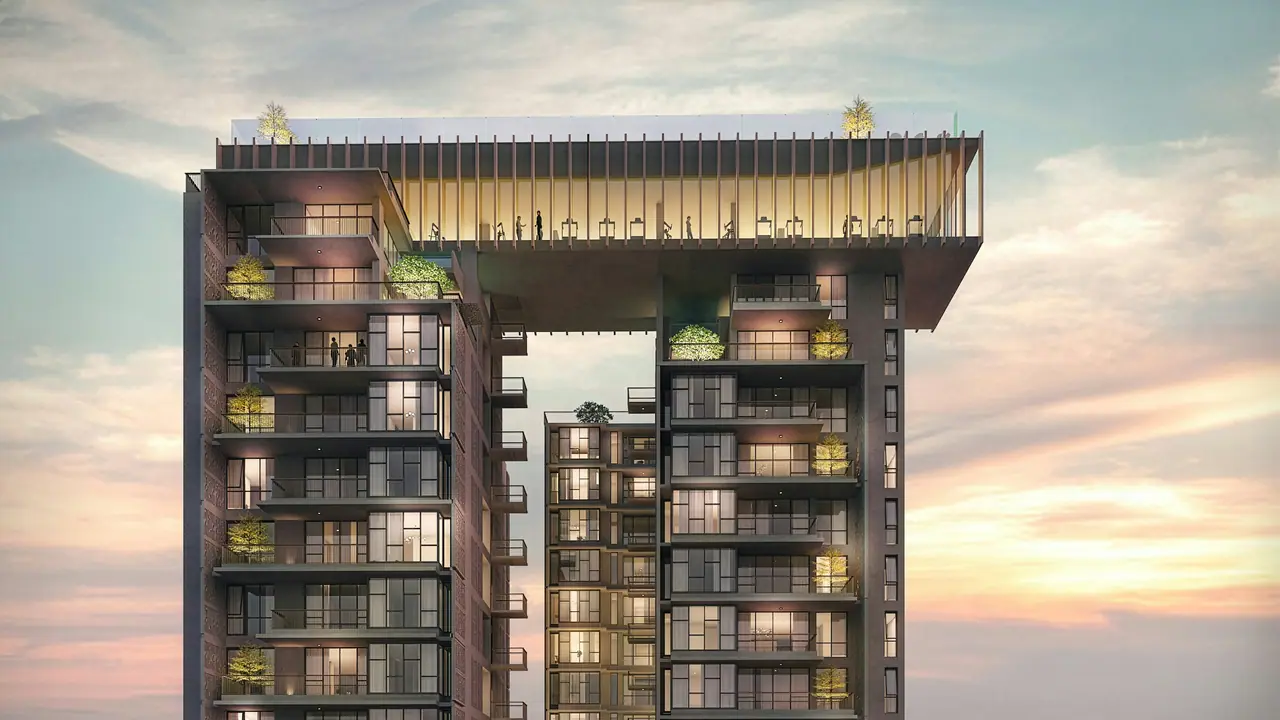 Two residential towers joined by a glass sky lounge, glowing at dusk